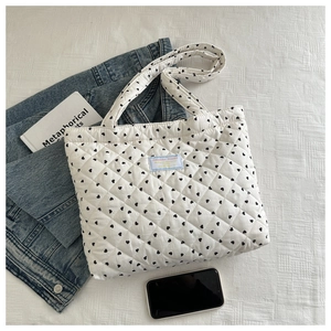 Detail of white quilted tote bag with black heart patterns and light blue woven label