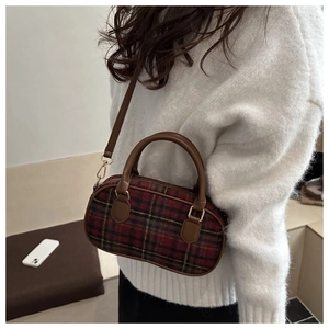 Detail of red and green plaid Boston bag with leather straps on a white knit sweater