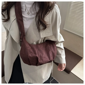 Détail d'un sac demi-lune en daim marron foncé plissé porté sur un trench-coat beige