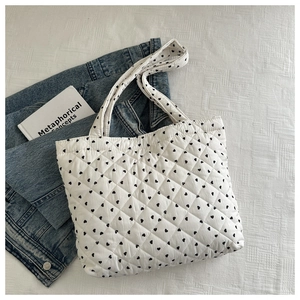 Detailed overhead shot of white quilted heart tote bag with denim and book on white fabric