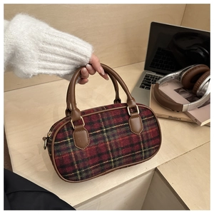 Close-up of red tartan cylinder handbag with brown leather handles on office desk