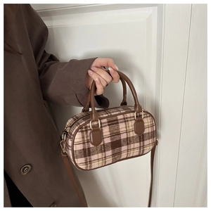 Close-up of pink plaid boston bag with brown leather handles and golden metal hardware