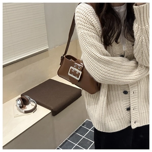 Détail d'un sac à bandoulière en cuir marron avec une grande boucle argentée sur le devant