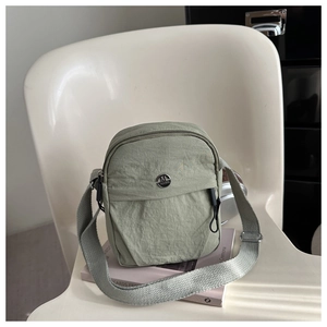 Close-up of sage green nylon crossbody bag with metallic logo and textured fabric