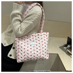 Detail of pink quilted tote bag featuring red heart patterns and brand woven label