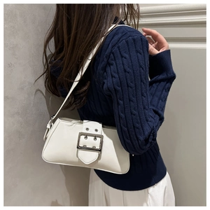 Detail view of white glossy underarm bag with silver buckle on blue knit sweater