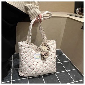 Detail of white quilted tote bag with red heart embroidery and cute cartoon plush charm