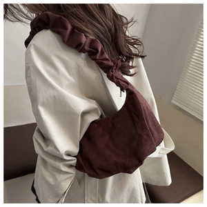 Détail du sac dumpling bordeaux avec bandoulière froncée sur blazer blanc
