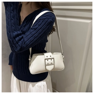 Detail of white matte leather shoulder bag with silver buckle on cable knit sweater