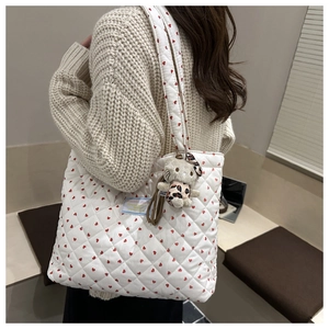 Detail of white quilted tote bag featuring red heart patterns and a plush cat pendant