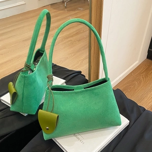 Green suede shoulder bag with long top handles and decorative charm in a mirror display