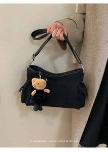 Detailweergave van zwarte schoudertas met zijzakken en schattige pluche hanger