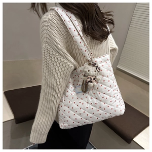 Detailed view of white quilted tote bag featuring red hearts and a plush cat charm