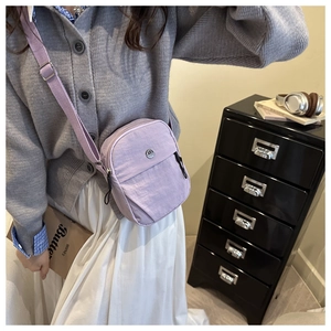 Close-up of a light purple nylon crossbody bag with adjustable fabric strap and metal logo