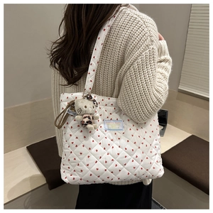 Detail of white quilted tote bag with red heart pattern and plush mascot accessory