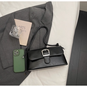 Détail du sac baguette rétro noir avec boucle fer à cheval argentée sur un veston chic
