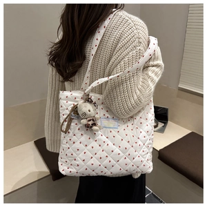 Detail of white quilted tote bag featuring red heart patterns and cute cat plush pendant