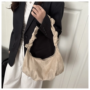 Sac croissant en daim beige avec anse plissée porté à l'épaule sur un blazer