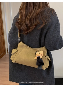 Detail van olijfgroene suède crossbodytas met zijzakken en een pluche kattenhanger