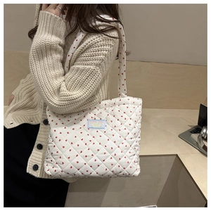 Close-up of white quilted tote bag with red heart pattern and brand label detail