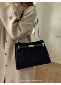 Détail du sac rétro en daim noir minimaliste avec fermoir doré sur un manteau beige