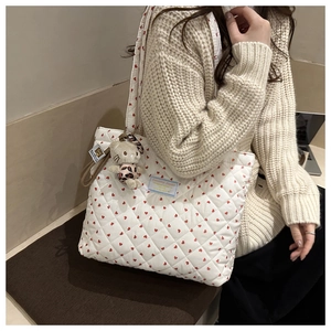 Close-up of a white quilted tote bag featuring red heart patterns and a plush charm