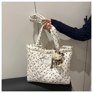 Detail of white quilted tote with black heart patterns and cute cat plush pendant charm
