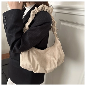Vue détaillée du sac nuage en daim beige avec anse froncée porté à l'épaule sur veste