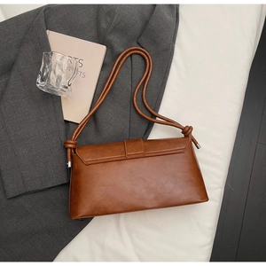 Detail of caramel brown retro baguette bag with knotted strap on a grey blazer