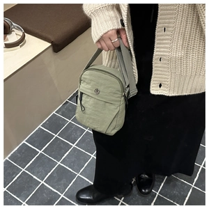 Close-up of bean green nylon mini crossbody bag with round M logo on white cardigan