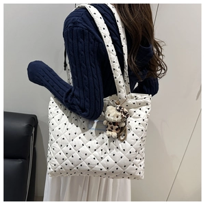 Detailed view of white quilted tote bag with black heart prints and plush charm