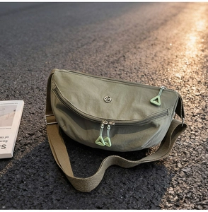 Detail of olive green nylon crescent bag with metal logo on asphalt road at sunset