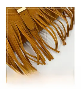 Macro detail of ginger suede tote bag featuring long fringes and a gold metal buckle