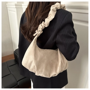 Détail du sac beige en velours avec bandoulière plissée sur veste de costume sombre