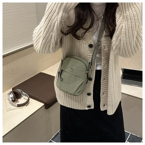 Detailed view of an olive green nylon crossbody bag with adjustable fabric strap and metal logo