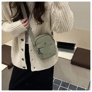 Detail view of light green crossbody bag with front zipper pocket on a beige cardigan