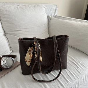 Large dark brown tote bag with white stitching and decorative silk scarf on a sofa