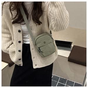 Detail view of sage green canvas crossbody bag with adjustable strap and metal logo