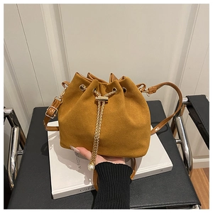 Detail of a brown suede bucket bag featuring a drawstring and gold chain with a pearl charm
