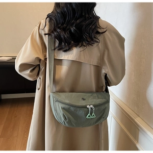 Close-up of a light green nylon crescent crossbody bag worn with a beige trench coat