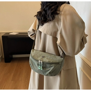 Detail of sage green nylon crescent bag with dual zippers and woven shoulder strap