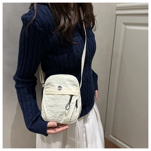Detail of white nylon shoulder bag featuring natural texture and round metal logo