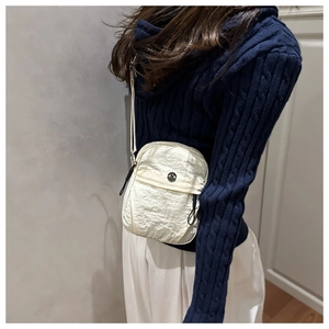 Detail of off-white nylon crossbody bag with black zipper pull and metallic logo on model