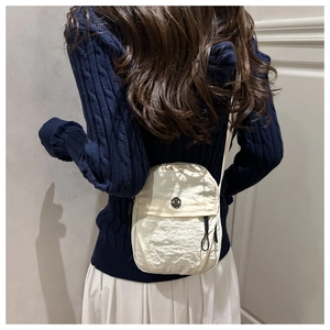 Close-up of a beige mini crossbody bag with a round silver logo on a textured fabric