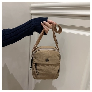 Detail of a beige nylon crossbody bag featuring a front pocket with a metal logo