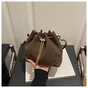 Detail of dark brown suede bucket bag featuring golden chain and pearl charm accents