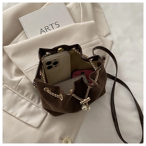 Detail of suede bucket bag showing drawstring chain, pearl charm and inner capacity