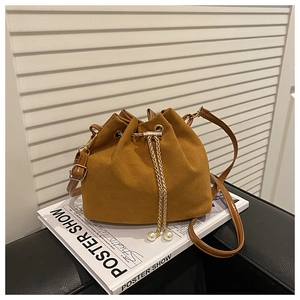 Close-up of brown suede bucket bag with gold chain and pearl pendants on magazine