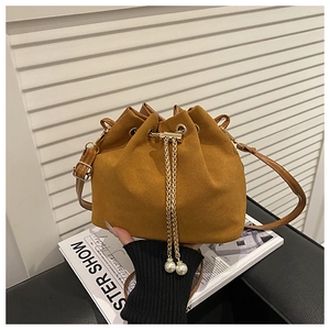 Detail of ginger suede bucket bag featuring elegant gold chain and pearl drawstring charms