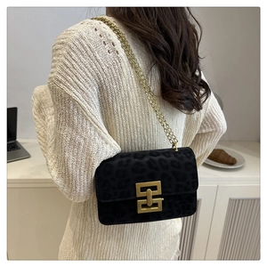 Detailed close-up of a leopard print flap bag with gold chain and metal lock on a table